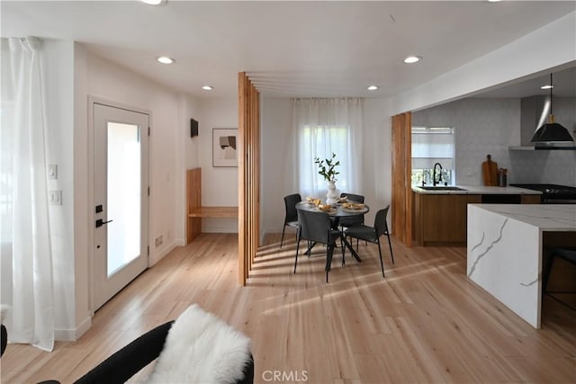 kitchen with light wood finished floors, brown cabinetry, wall chimney exhaust hood, modern cabinets, and a sink