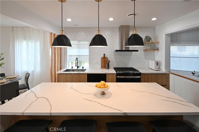 kitchen featuring black dishwasher, brown cabinetry, stove, wall chimney range hood, and a sink