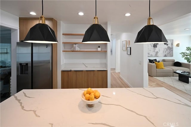 kitchen with brown cabinetry, modern cabinets, light stone counters, fridge with ice dispenser, and light wood-type flooring