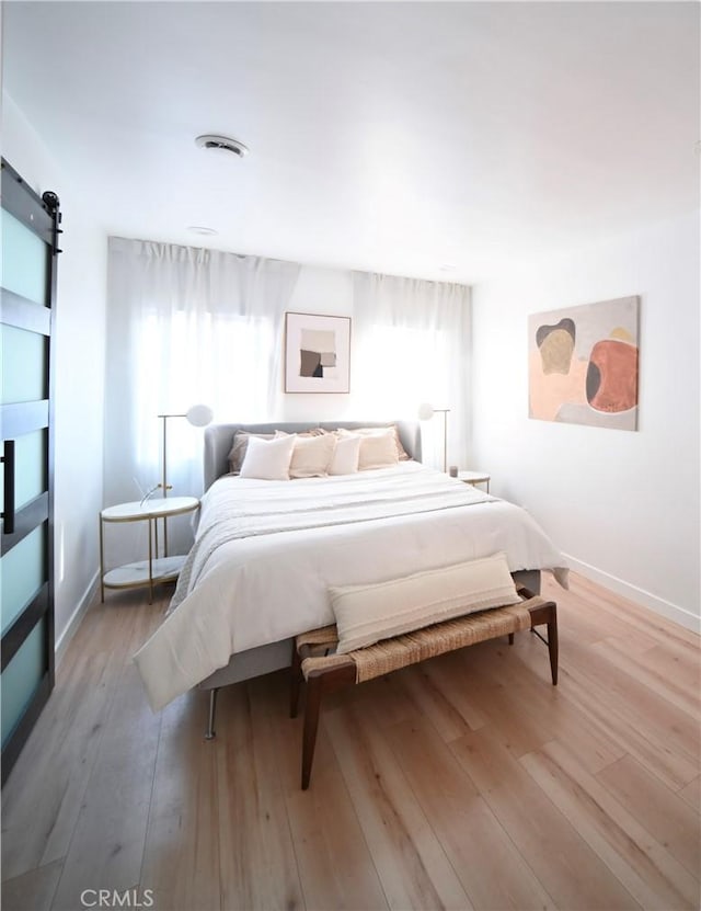 bedroom with light wood-style flooring, baseboards, and a barn door