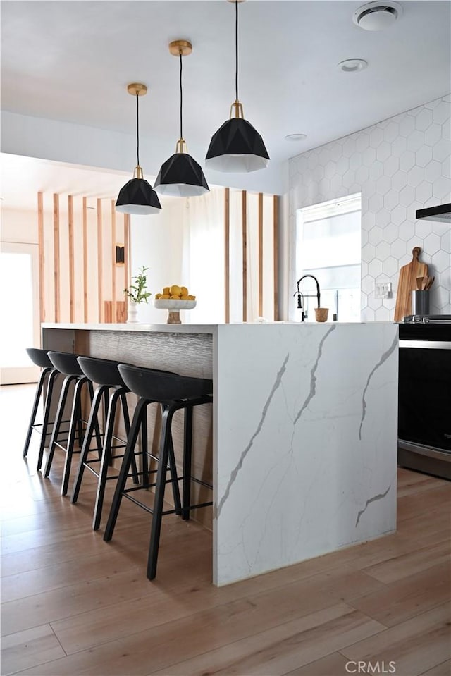 kitchen with light wood-type flooring, light stone countertops, range, and decorative light fixtures