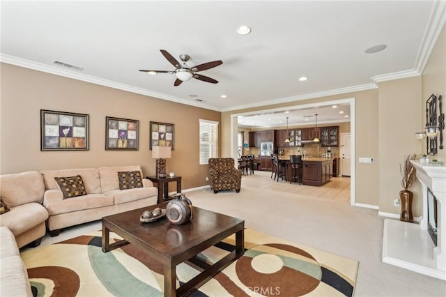 living area featuring visible vents, a fireplace with raised hearth, crown molding, baseboards, and light colored carpet