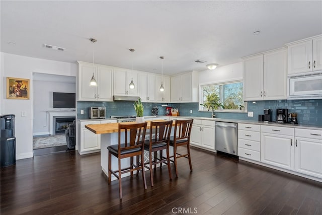 kitchen with visible vents, white cabinets, white microwave, under cabinet range hood, and stainless steel dishwasher