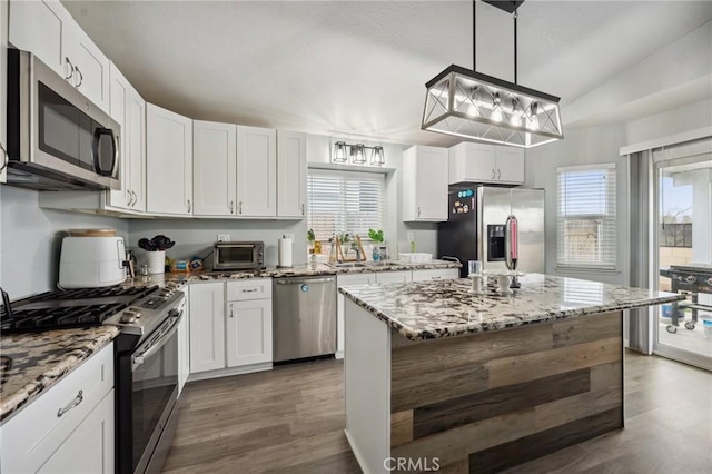 kitchen with light stone counters, dark wood-style flooring, white cabinetry, hanging light fixtures, and appliances with stainless steel finishes