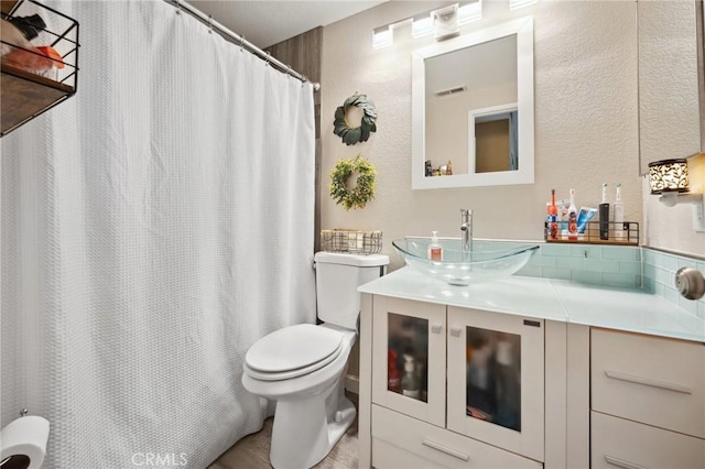 full bathroom with toilet, a textured wall, vanity, and visible vents