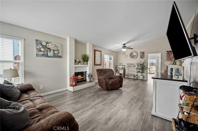 living area with a wealth of natural light, vaulted ceiling, a fireplace, and wood finished floors