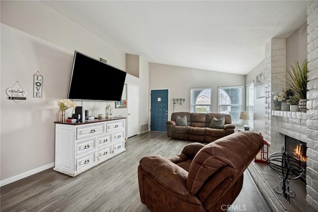 living area featuring a large fireplace, baseboards, visible vents, lofted ceiling, and wood finished floors