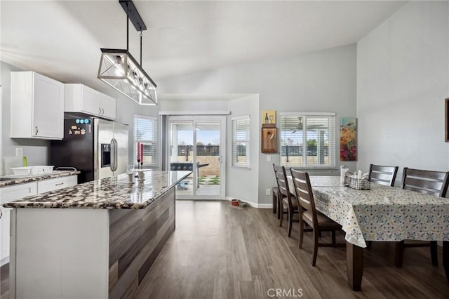 kitchen with white cabinetry, a kitchen island, wood finished floors, dark stone counters, and stainless steel fridge