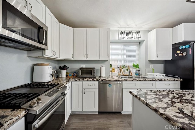 kitchen with stainless steel appliances, dark stone counters, white cabinets, and a sink