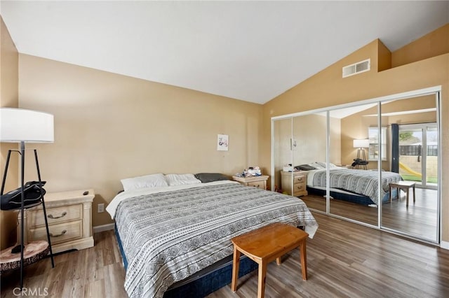 bedroom with a closet, visible vents, vaulted ceiling, and wood finished floors