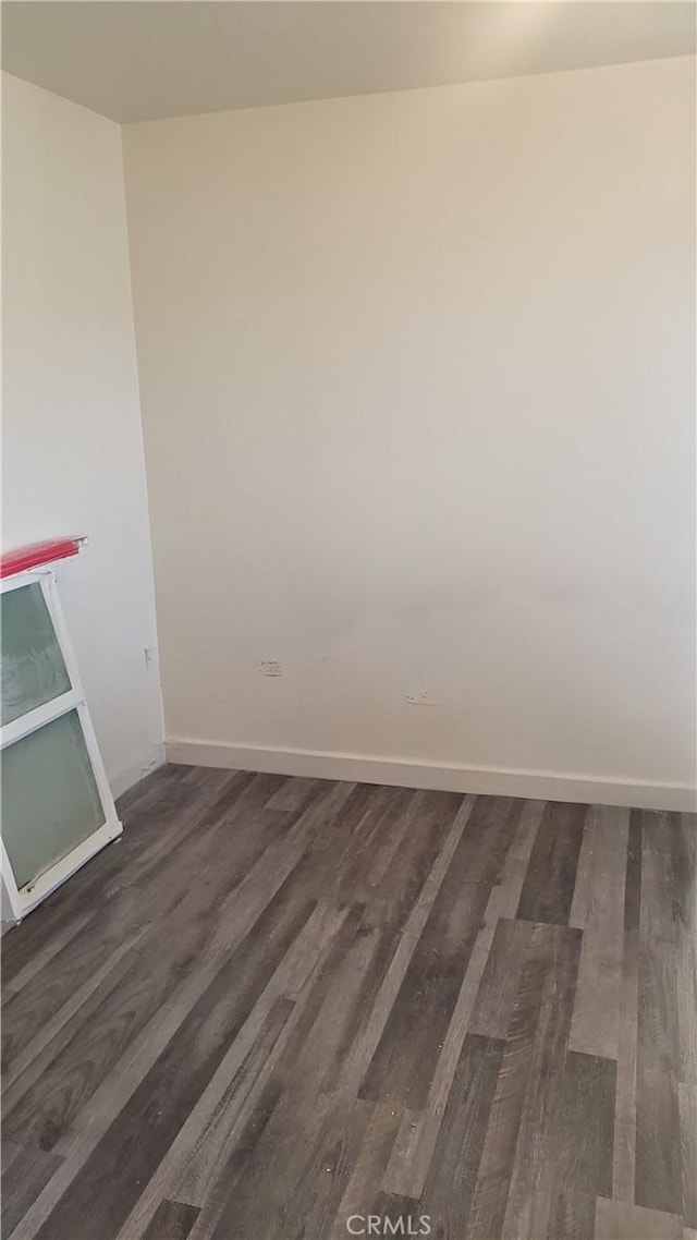 spare room featuring baseboards and dark wood finished floors