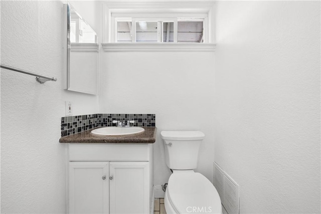 half bath featuring backsplash, visible vents, vanity, and toilet