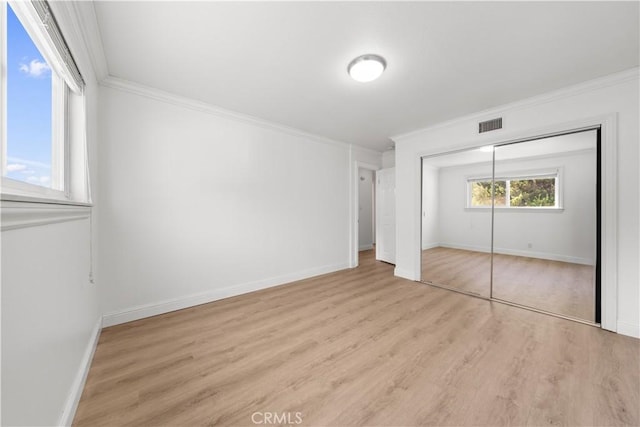 unfurnished bedroom with baseboards, visible vents, ornamental molding, wood finished floors, and a closet