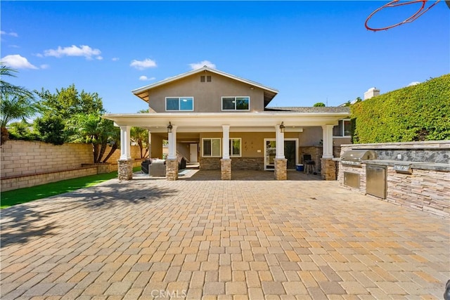 view of front of house with stucco siding, area for grilling, a patio area, fence, and stone siding