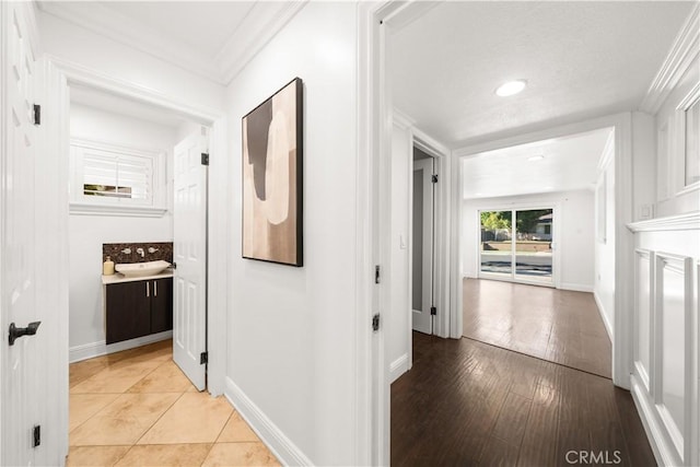 hallway with ornamental molding, light wood-style flooring, and baseboards