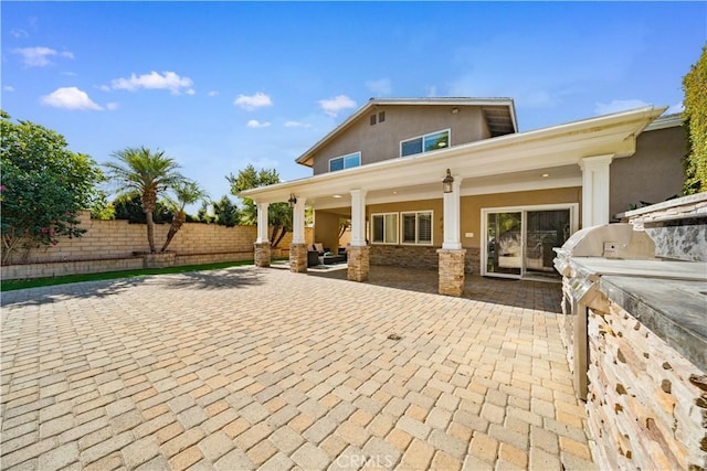 back of house with stone siding, fence, area for grilling, and stucco siding