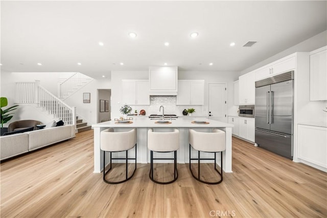 kitchen with stainless steel built in refrigerator, white cabinets, a sink, and a kitchen bar