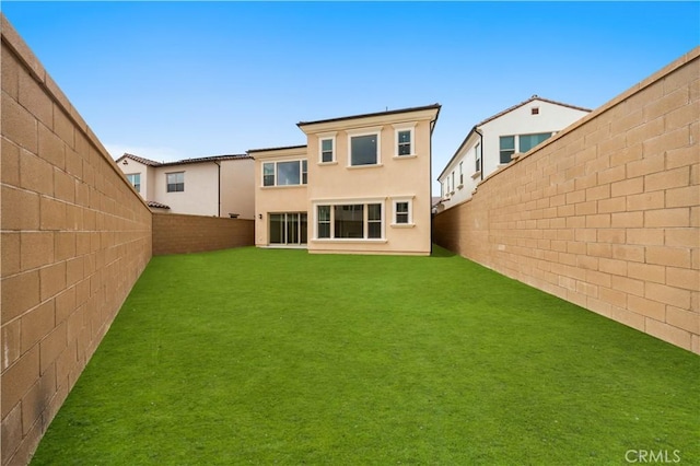 back of property with a fenced backyard, a yard, and stucco siding