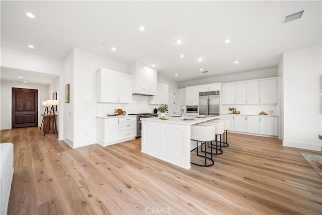 kitchen with an island with sink, light wood finished floors, high end appliances, and a kitchen breakfast bar