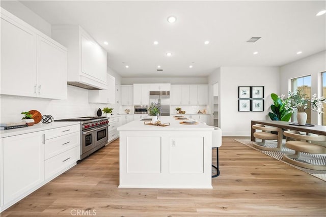 kitchen with recessed lighting, light countertops, light wood-style flooring, white cabinets, and high quality appliances