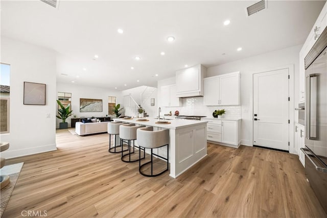 kitchen featuring visible vents, decorative backsplash, white cabinets, light wood-style flooring, and a breakfast bar area