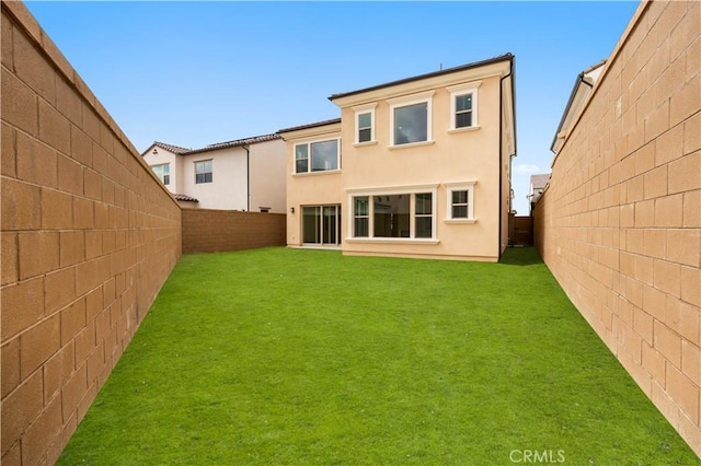 rear view of property with a yard, a fenced backyard, and stucco siding