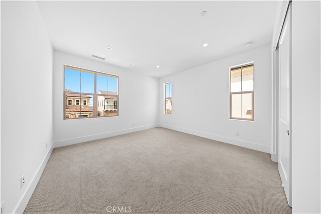 empty room featuring light carpet, visible vents, baseboards, and recessed lighting