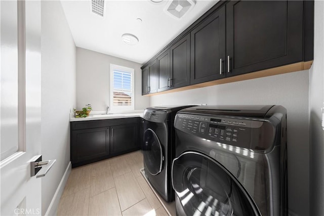 washroom with a sink, visible vents, baseboards, cabinet space, and washing machine and clothes dryer