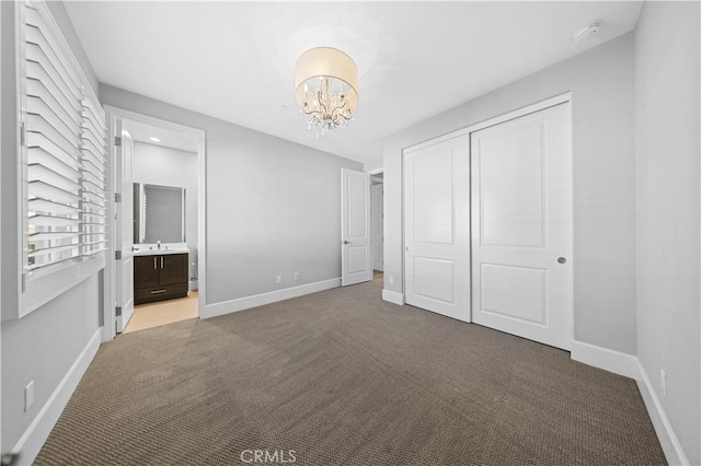 unfurnished bedroom featuring baseboards, ensuite bath, an inviting chandelier, carpet floors, and a closet