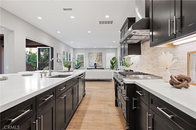 kitchen with tasteful backsplash, light countertops, visible vents, a sink, and wall chimney range hood