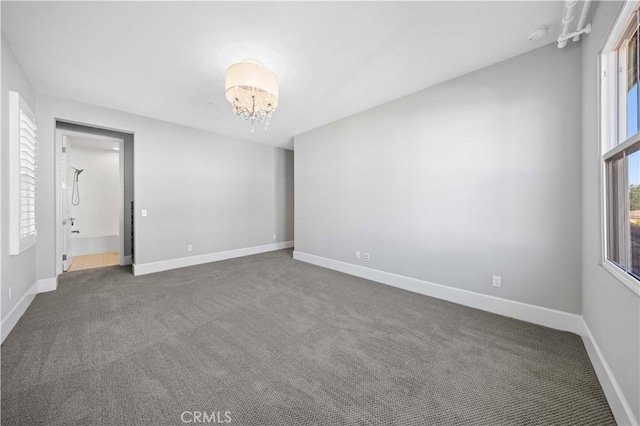 empty room featuring dark colored carpet, a notable chandelier, and baseboards