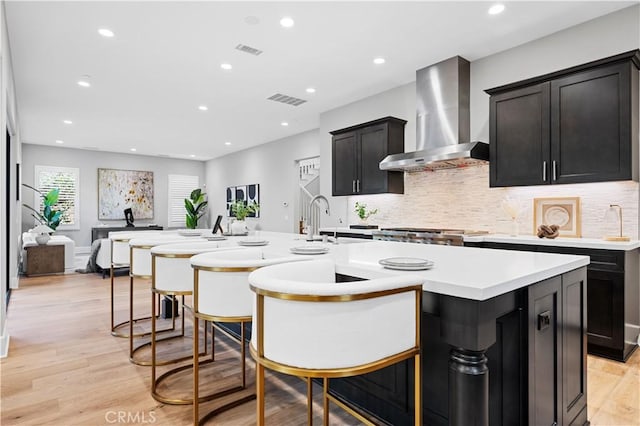 kitchen with light wood-type flooring, wall chimney range hood, a kitchen bar, and visible vents