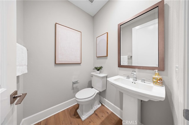 half bathroom featuring wood finished floors, toilet, and baseboards