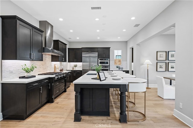 kitchen featuring visible vents, light countertops, appliances with stainless steel finishes, wall chimney exhaust hood, and light wood finished floors