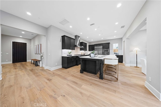 kitchen featuring visible vents, wall chimney exhaust hood, dark cabinets, stainless steel built in refrigerator, and light countertops