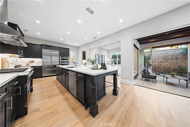 kitchen with appliances with stainless steel finishes, light countertops, dark cabinetry, and wall chimney exhaust hood