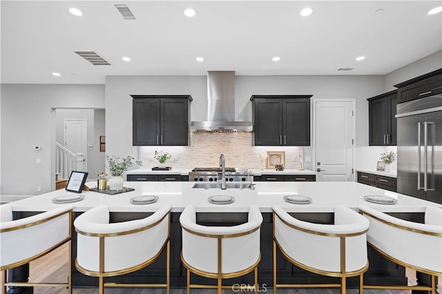 kitchen featuring visible vents, decorative backsplash, wall chimney exhaust hood, built in refrigerator, and light countertops