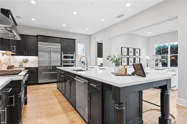 kitchen featuring appliances with stainless steel finishes, a breakfast bar, extractor fan, light countertops, and a sink