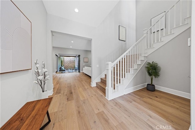 entrance foyer with recessed lighting, wood finished floors, a towering ceiling, baseboards, and stairs