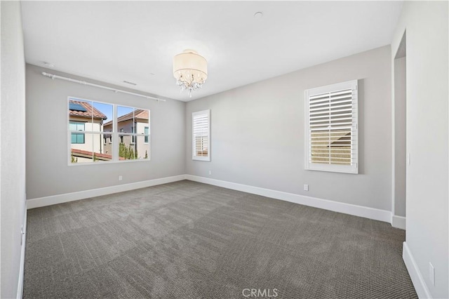 empty room with dark colored carpet, a notable chandelier, and baseboards