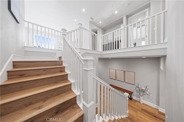 staircase with a high ceiling, recessed lighting, wood finished floors, and baseboards