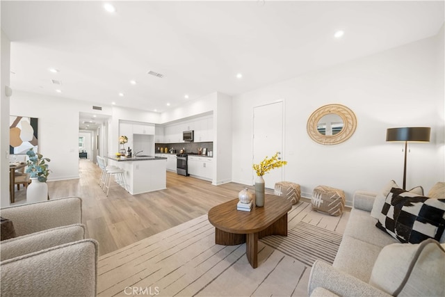 living room with light wood finished floors, baseboards, visible vents, and recessed lighting