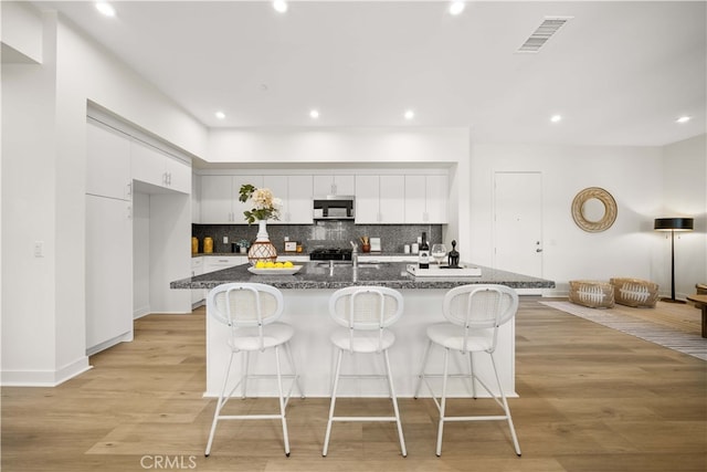 kitchen featuring a breakfast bar area, visible vents, white cabinets, light wood-style floors, and tasteful backsplash