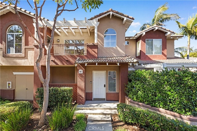 townhome / multi-family property with a tiled roof, a balcony, and stucco siding