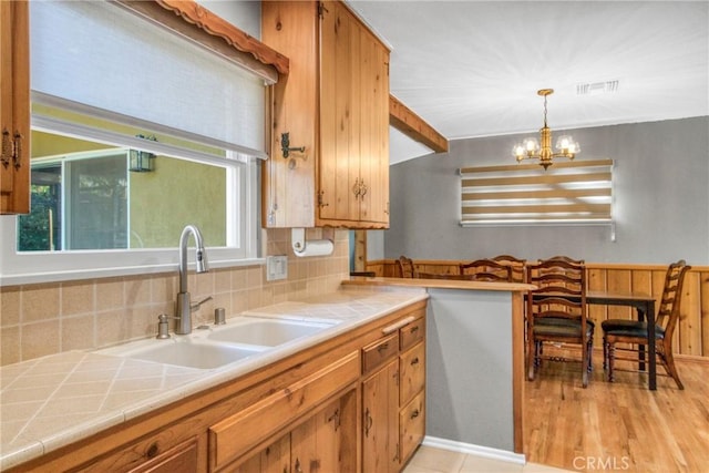 kitchen with a chandelier, a sink, tile counters, and brown cabinets