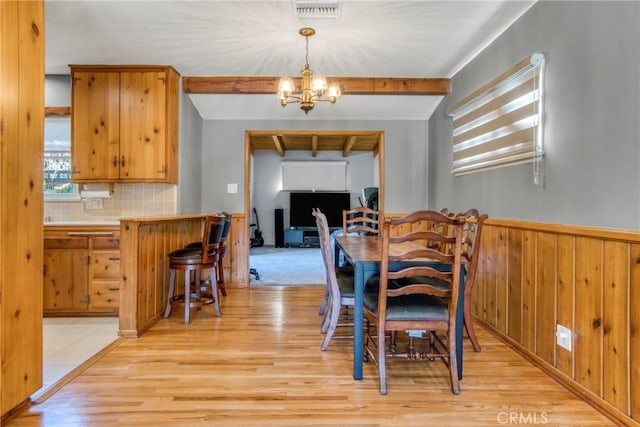 dining area with a chandelier, visible vents, wainscoting, light wood finished floors, and beamed ceiling