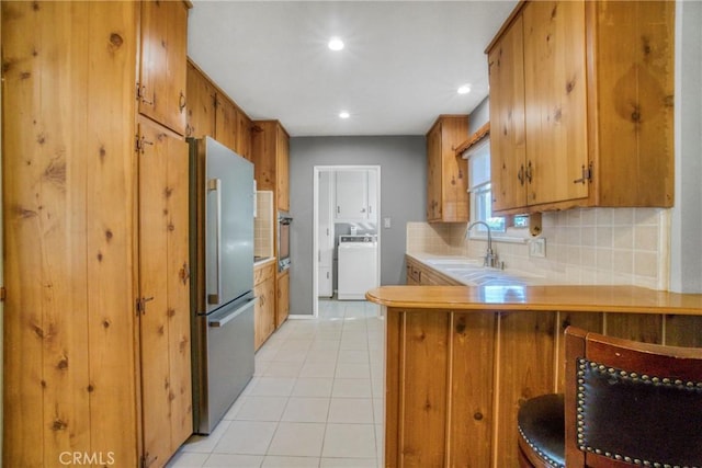 kitchen featuring washer / clothes dryer, brown cabinetry, a sink, and freestanding refrigerator