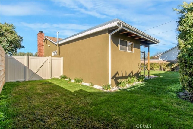 view of side of home featuring a gate, a yard, fence, and stucco siding