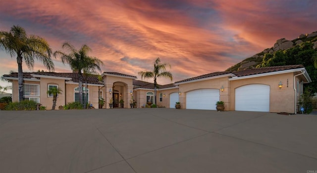 mediterranean / spanish-style house with an attached garage, a tile roof, concrete driveway, and stucco siding