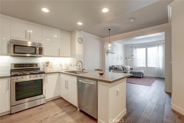 kitchen with appliances with stainless steel finishes, open floor plan, white cabinets, a sink, and a peninsula